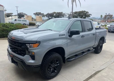 A gray Chevrolet Z71 pickup truck with black wheels is parked on a concrete driveway near palm trees.